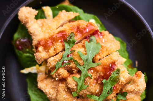 Fried chicken in breadcrumbs with tomato sauce and salad greens on black plate in cafe