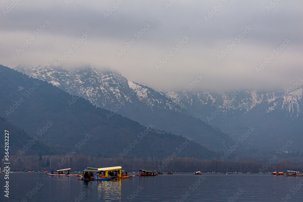 Kashmir, Srinagar India - Jan 10 2023: Popular Srinagar Houseboats in Dal Lake. Colorful Shikara ride floating in Dal Lake aka Nigeen lake. Mountain range in Srinagar. Couple Honeymoon Destination. 