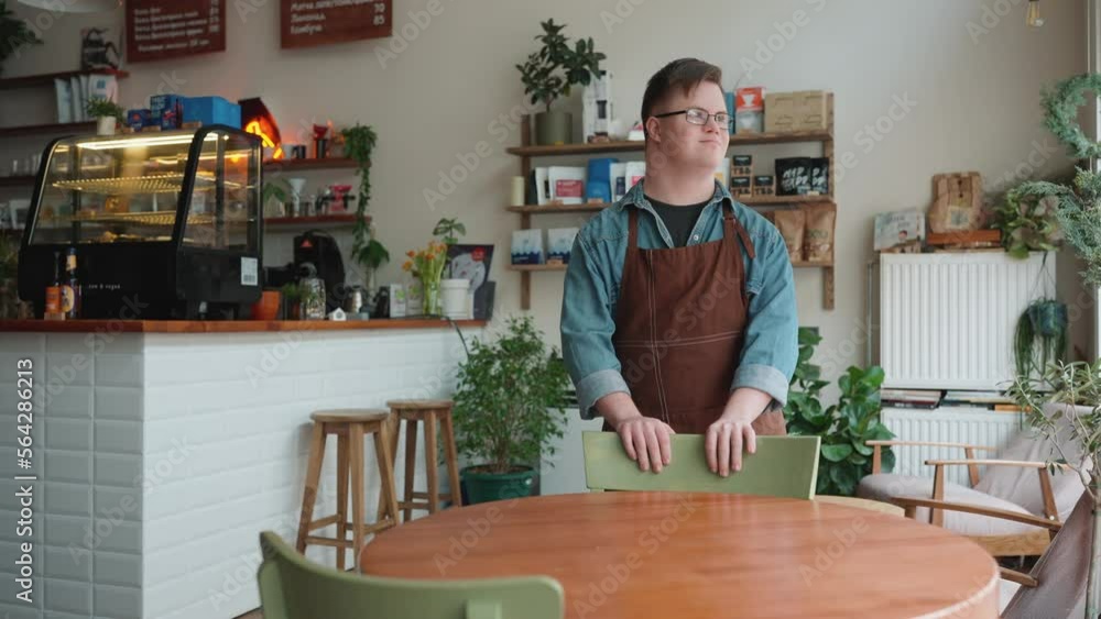 Positive man barista with Down syndrome looking at window while standing in cafe Positive man barista with Down syndrome looking at window while standing in cafe