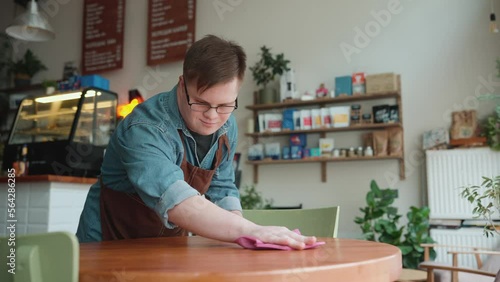 Positive man barista with Down syndrome wiping table in cafe