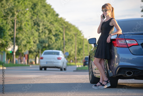 Stylish woman driver standing near her vehicle talking on cellphone on city street in summer © bilanol