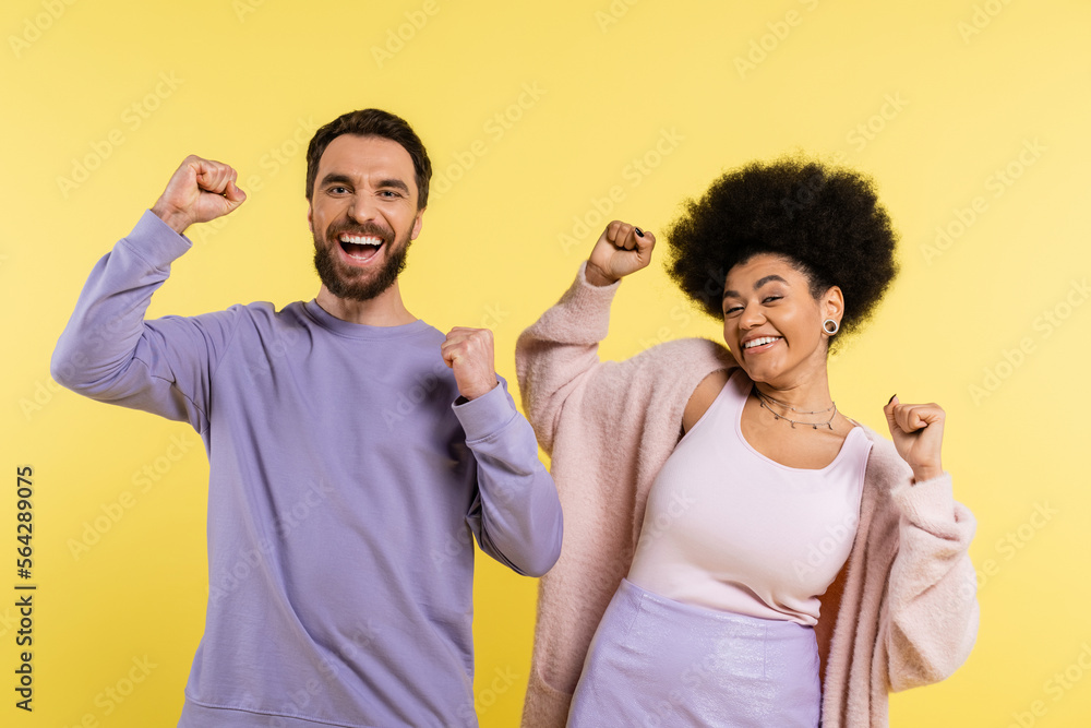 excited interracial couple looking at camera and celebrating success isolated on yellow. excited interracial couple looking at camera and celebrating success isolated on yellow.