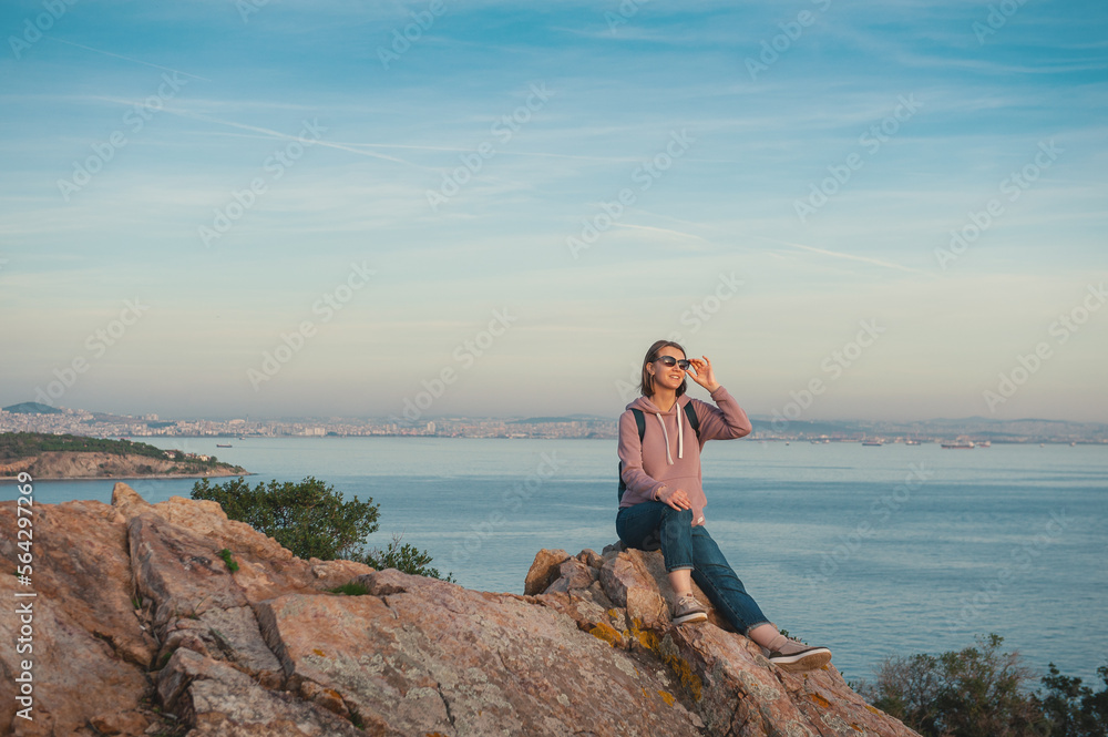 Young beautiful woman wearing eyeglasses looking on the sunlight sit on the rock over the sea Young beautiful woman wearing eyeglasses looking on the sunlight sit on the rock over the sea