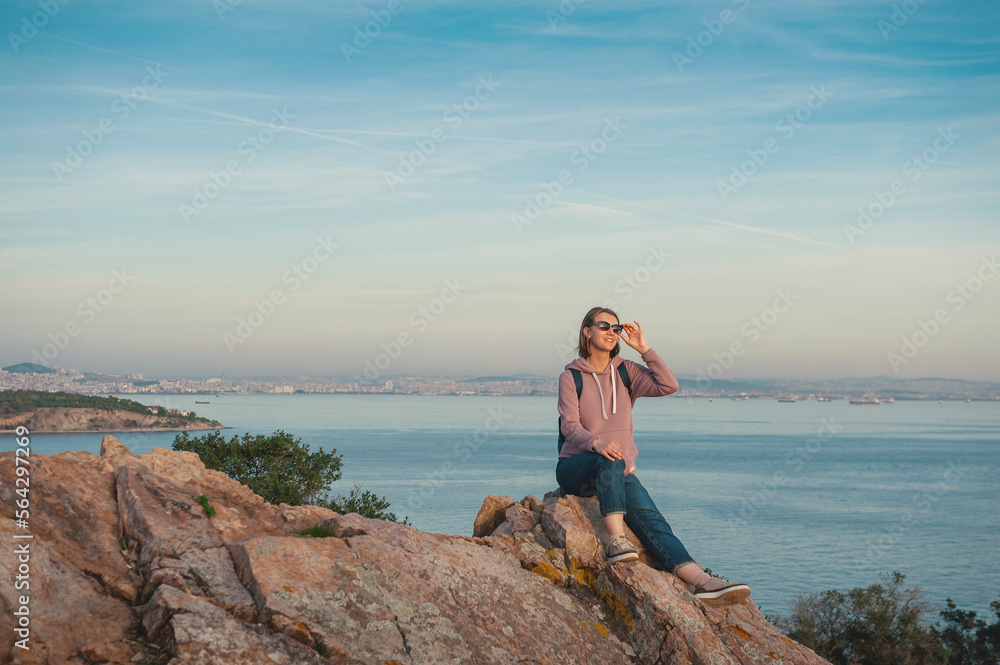 Young beautiful woman wearing eyeglasses looking on the sunlight sit on the rock over the sea