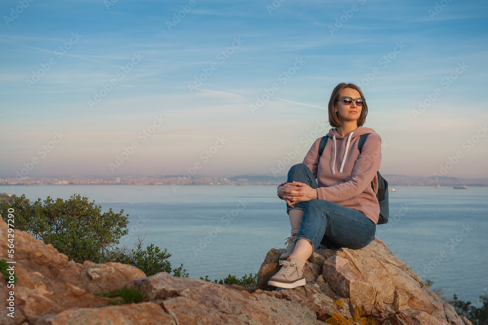 Young beautiful woman wearing eyeglasses looking on the sunlight sit on the rock over the sea Young beautiful woman wearing eyeglasses looking on the sunlight sit on the rock over the sea