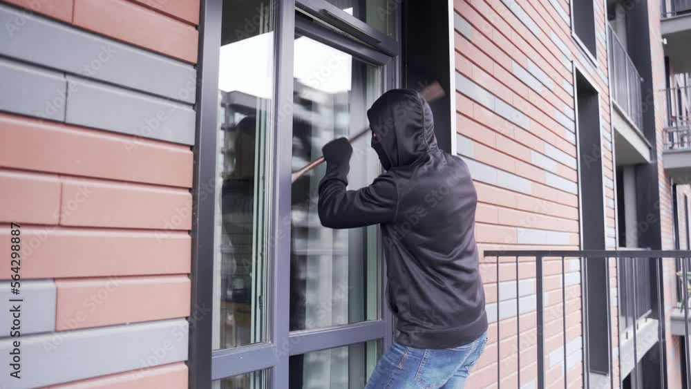 A thief sneaks into the apartment through the courtyard or balcony. A man in a black jacket and mask looks into the room through the glass door, breaks it open with a crowbar and enters the room A thief sneaks into the apartment through the courtyard or balcony. A man in a black jacket and mask looks into the room through the glass door, breaks it open with a crowbar and enters the room