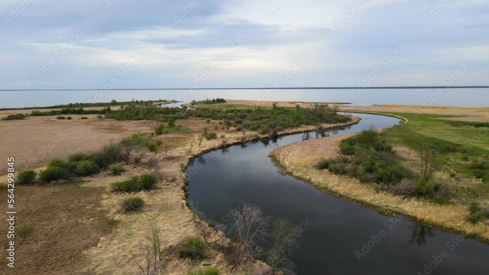 Aerial moving forward above a winding calm river towards a large lake. The river is surrounded by dry looking marsh grass and scattered trees.
Aerial moving forward above a winding calm river towards a large lake. The river is surrounded by dry looking marsh grass and scattered trees.