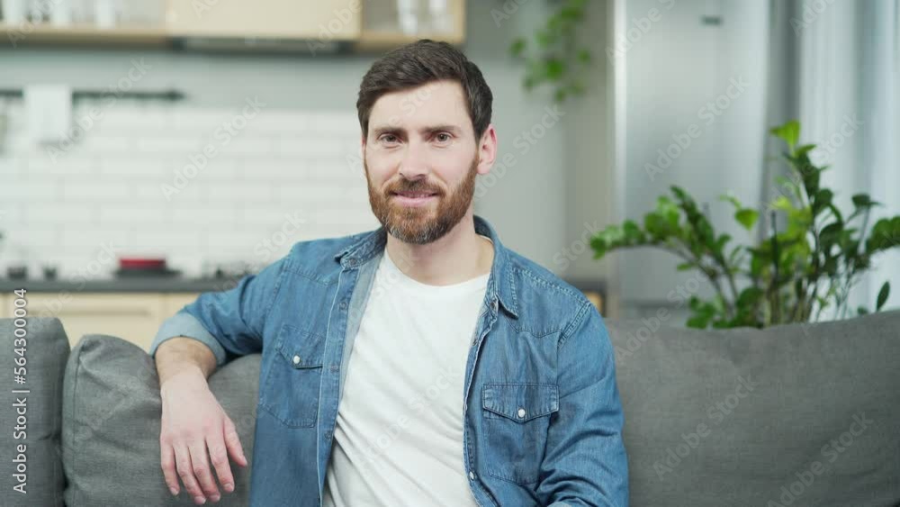 Close-up portrait of mature сaucasian man with beard smiling and looking at camera while sitting on couch in living room Confident handsome male in casual clothes relaxing on sofa in kitchen at home Close-up portrait of mature сaucasian man with beard smiling and looking at camera while sitting on couch in living room Confident handsome male in casual clothes relaxing on sofa in kitchen at home