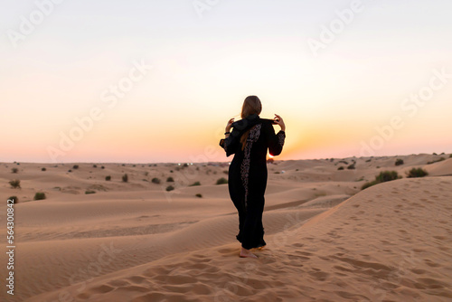 Back view of Beautiful mysterious woman in traditional arabic black long dress stands in the desert on sunset © bondvit