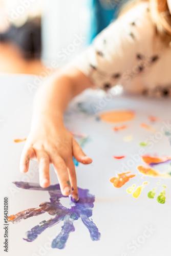 A little girl painting with her hands on a white sheet of paper.