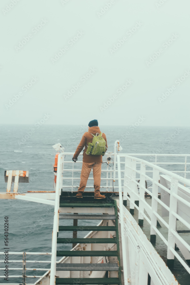 Back view of the tourist man with backpack aboard a ferry looking around. Male enjoying the view before the shipping. Back view of the tourist man with backpack aboard a ferry looking around. Male enjoying the view before the shipping.