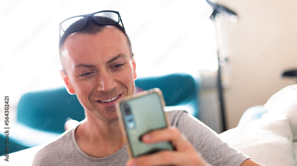 The adult man is smiling while looking at his mobile phone.