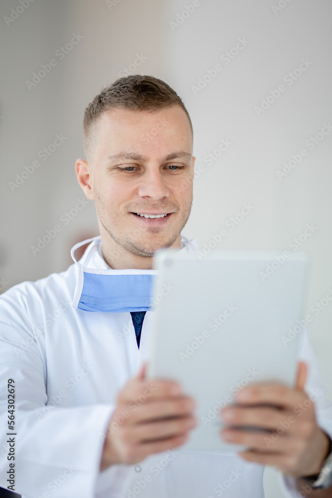 Doctor with a mask and glasses looking at his tablet and smiling Doctor with a mask and glasses looking at his tablet and smiling