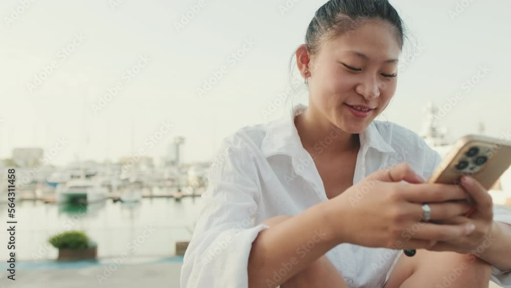 Close up, smiling young woman using mobile phone on seascape background Close up, smiling young woman using mobile phone on seascape background