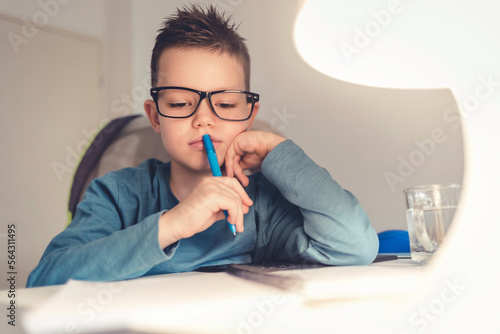 Boy sits at desk in the living room with computer doing homework during the day. Shot of a determined young boy doing his homework at home