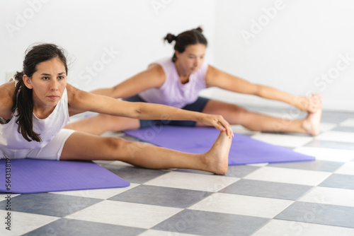 Preparation for Upavistha Konasana pose. Two Latin women practicing yoga. Close up and selective focus image. Wellbeing and body care concept