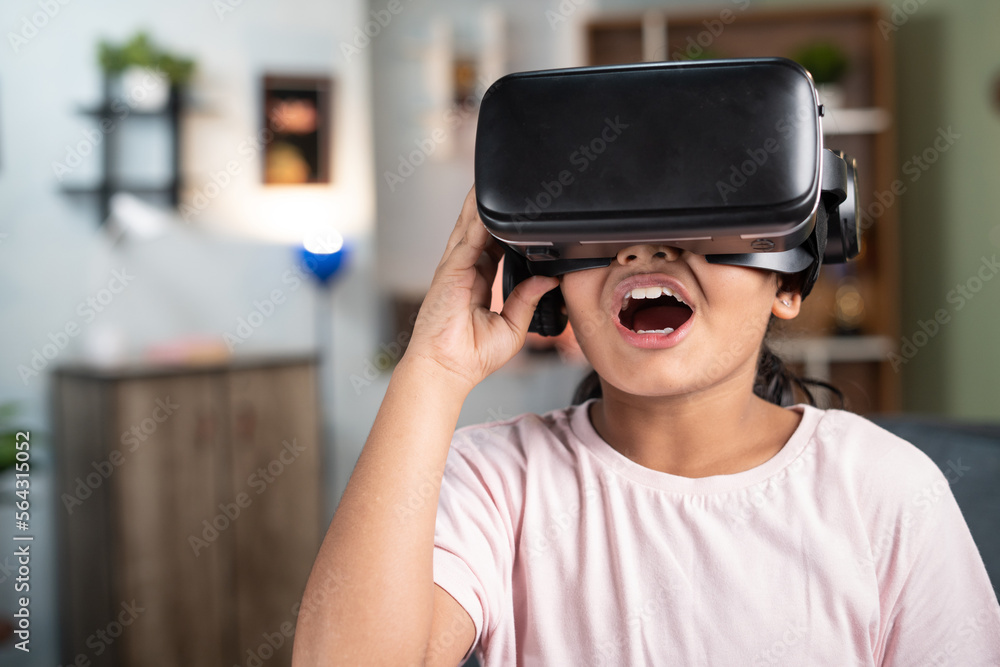 Excited girl kid with VR or vertual reality headset experiencing metaverse at home - concept of immersive experience and modern technology Excited girl kid with VR or vertual reality headset experiencing metaverse at home - concept of immersive experience and modern technology