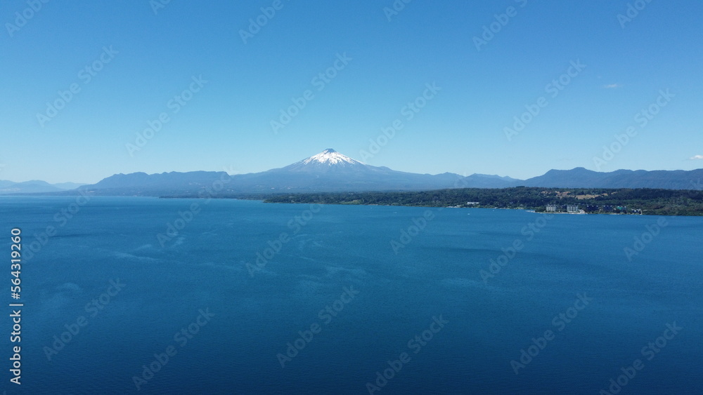 Aerial view of the volcano and mountains, on the shore of a lake in summer, with the city in the distance.