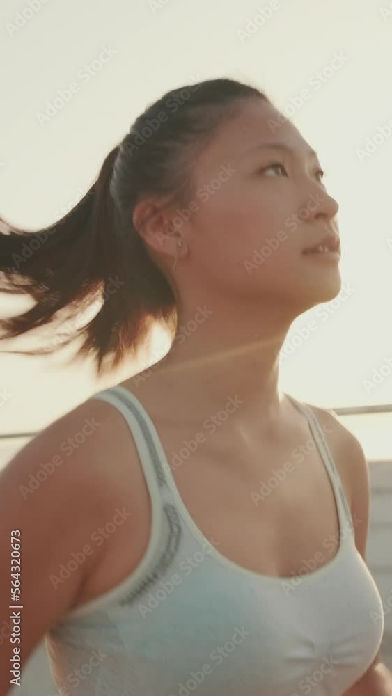 VERTICAL VIDEO: Asian girl in sports top runs along the promenade at morning time VERTICAL VIDEO: Asian girl in sports top runs along the promenade at morning time