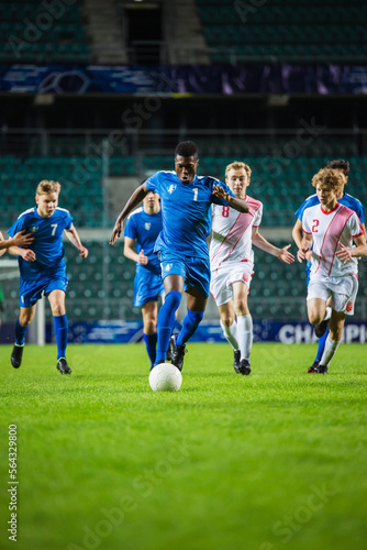 Vertical Shot of Professional Soccer Football Match Championship: Blue Team Attacks, Black Forward Masterfully Dribbles on an International Tournament. Television Channel Broadcast. © Gorodenkoff