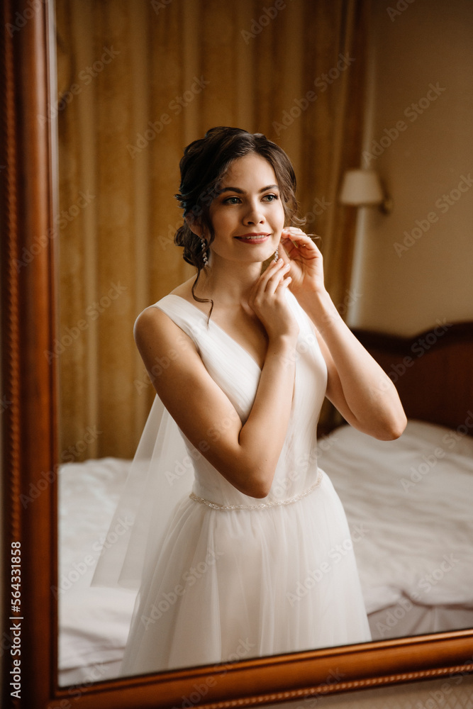 bride puts on earrings in the reflection of the mirror