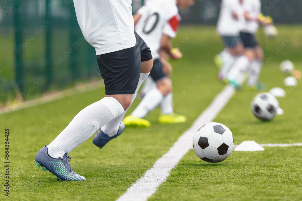 Group of soccer players kicking balls on training drill along sideline. Football training camp for youth. Footballers improving skills at training pitch