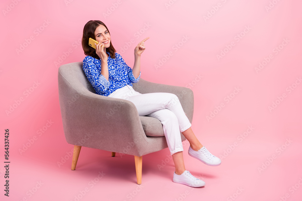 Full length photo of shiny dreamy lady wear print shirt talking modern device pointign empty space isolated pink color background Full length photo of shiny dreamy lady wear print shirt talking modern device pointign empty space isolated pink color background