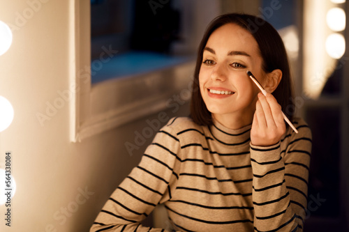 Happy beautiful young lady aplying makeup at home photo