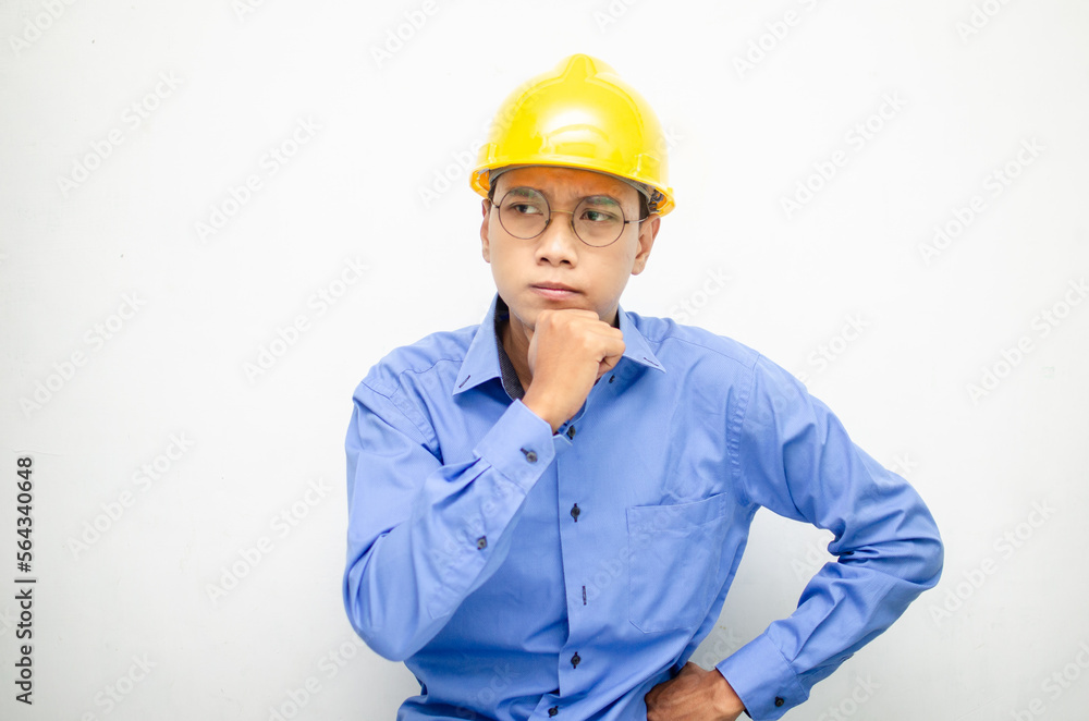 Asian construction worker in blue shirt and yellow safety helmet is seriously thinking with a wondering and thinking gesture and expression. Asian construction worker in blue shirt and yellow safety helmet is seriously thinking with a wondering and thinking gesture and expression.