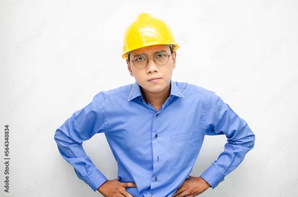 asian male construction worker or engineer in blue shirt and safety yellow helmet shows expresion of anger, furious and dissapointment isolated over white. stressed over work concept asian male construction worker or engineer in blue shirt and safety yellow helmet shows expresion of anger, furious and dissapointment isolated over white. stressed over work concept