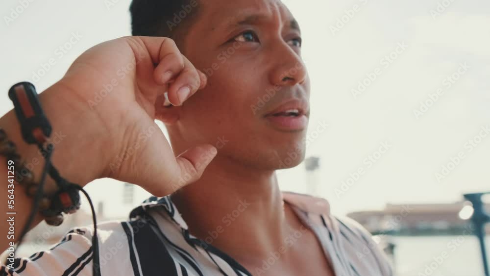 Close up, young man tourist sits on bench on the pier talking using headset Close up, young man tourist sits on bench on the pier talking using headset
