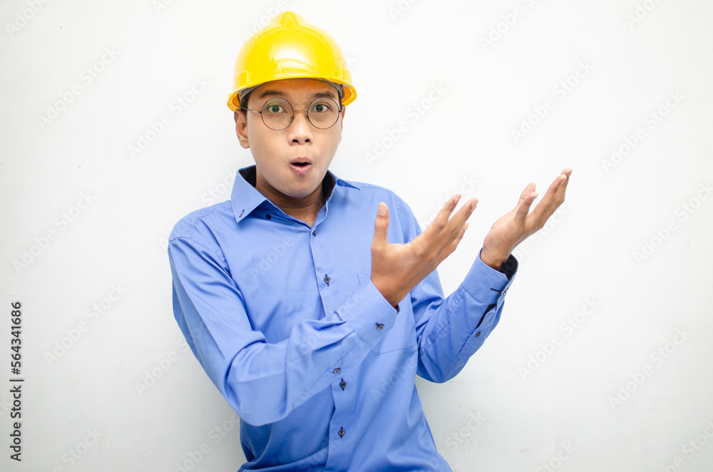 A happy, shocked asian consrtuction worker in blue shirt and yellow safety helmet pointing finger and presenting something ads. 