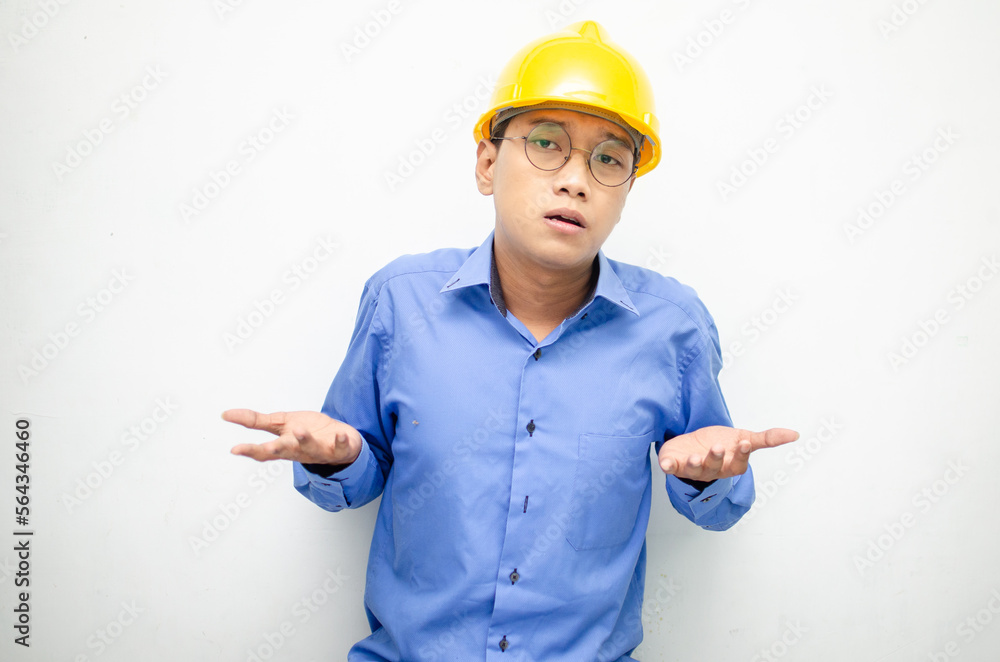 Young Asian man construction worker in yellow safety helmet unsure of what to choose with hand pointing left or right, isolated over whote background. advertising model for billboards. Young Asian man construction worker in yellow safety helmet unsure of what to choose with hand pointing left or right, isolated over whote background. advertising model for billboards.