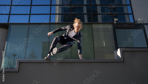 businessman jumping doing parkour with long blonde hair and glasses executive business clothes