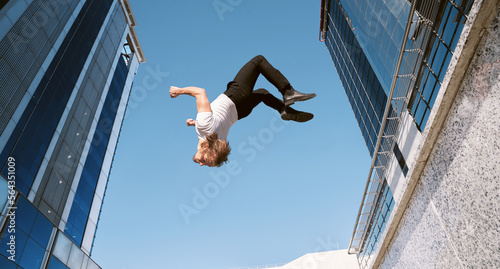 caucasian blond boy doing a backflip and parkour with blue sky in the background