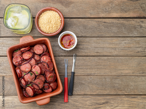 Grilled calabrese sausage portion with onion, farofa and caipirinha over wooden table with copy space photo