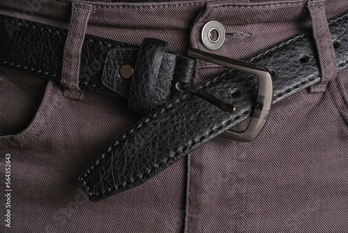 Unbuttoned black, male leather belt worn on jeans.
