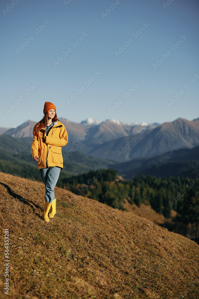 Naklejka premium Woman walking full-length on a hill in the autumn and looking out at the mountains in a yellow raincoat and jeans happy camping trip, freedom lifestyle 