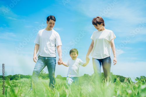 手を繋いで晴天の緑地を歩く親子3人  © maru54