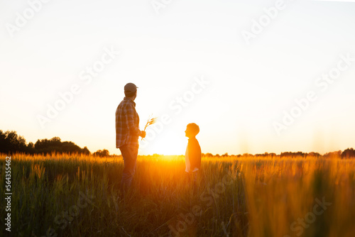 Farmer and his son in front of a sunset agricultural landscape. Man and a boy in a countryside field. Fatherhood  country life  farming and country lifestyle concept.
