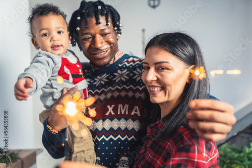 Smiling multicultural parents and their toddler with Christmas sparkling fire sticks. High quality photo
