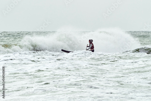 Photography Young courageous athlete woman surfing by wave on stand up paddle board and catching waves at winter period in sea