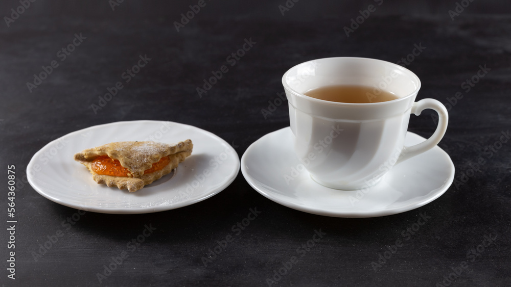 On the table are a cup of tea and cookies. On a dark background. Horizontal frame. On the table are a cup of tea and cookies. On a dark background. Horizontal frame.