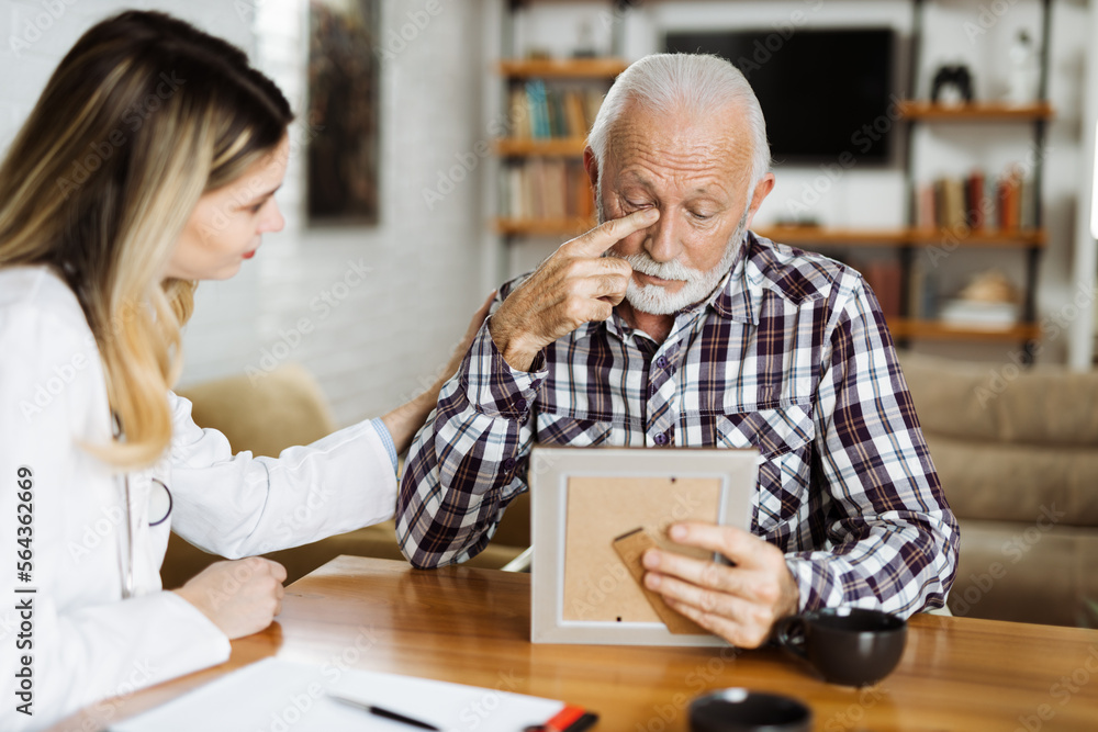Female home caregiver comforting senior man who is talking about his old photo at home Female home caregiver comforting senior man who is talking about his old photo at home