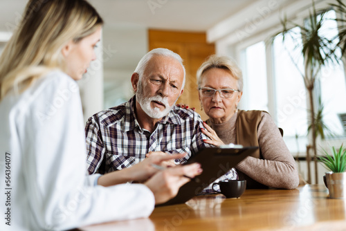 Mature couple looking at their plan of care and medications with female nurse at home photo