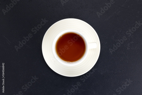 A cup of black hot tea in a white ceramic mug on a black background. Top view.
