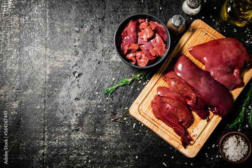 Raw liver on a cutting board with rosemary and spices. 