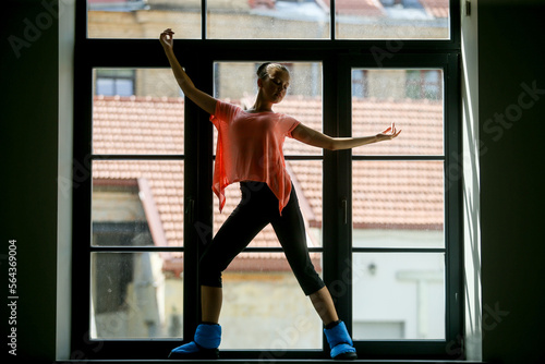 Silhouette of a young ballerina on the window sill, roof in the background. Concept of healthy lifestyle