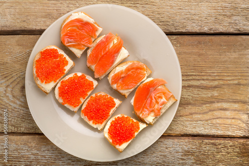 Toasts with red caviar and trout and butter on a plate on a wooden table.