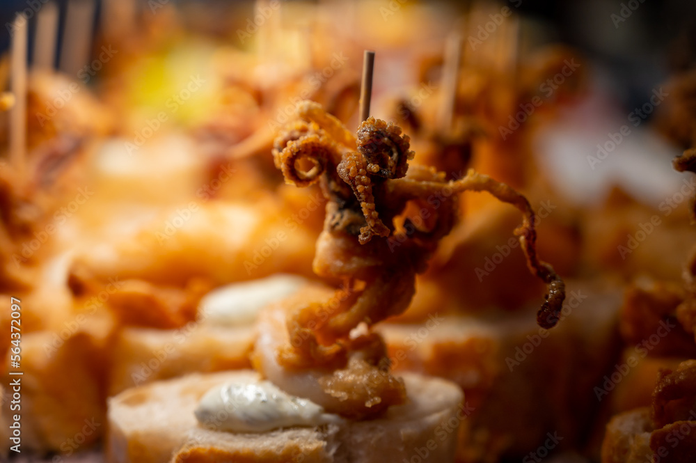 Fototapeta premium Typical snack of Basque Country, pinchos or pinxtos skewers with small pieces of bread, sea food, baby octopus, cheese, jamon served in bar in San-Sebastian or Bilbao, Spain